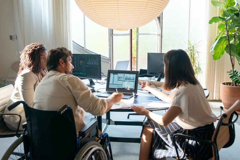 Shot from behind of three people having a meeting at a round table, one of whom is a wheelchair user