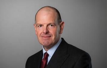 Head and shoulders shot of Neil Unsworth wearing a dark charcoal suit and red tie 